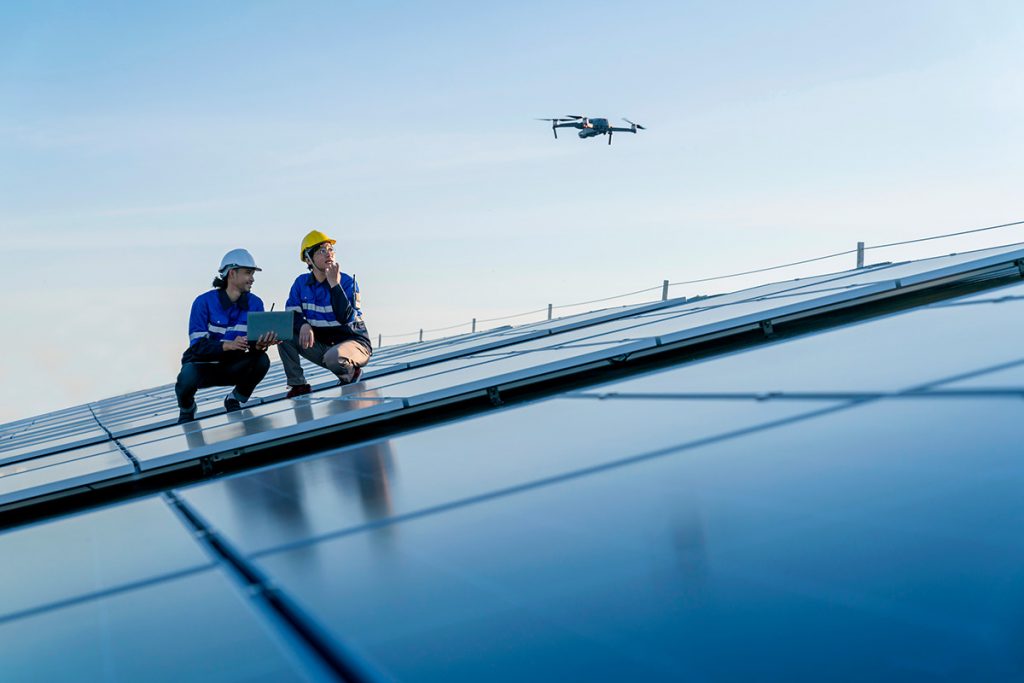 Specialist technician professional engineercontrol drone checking top view of installing solar roof panel on the factory rooftop under sunlight. Engineers holding tablet check solar roof.