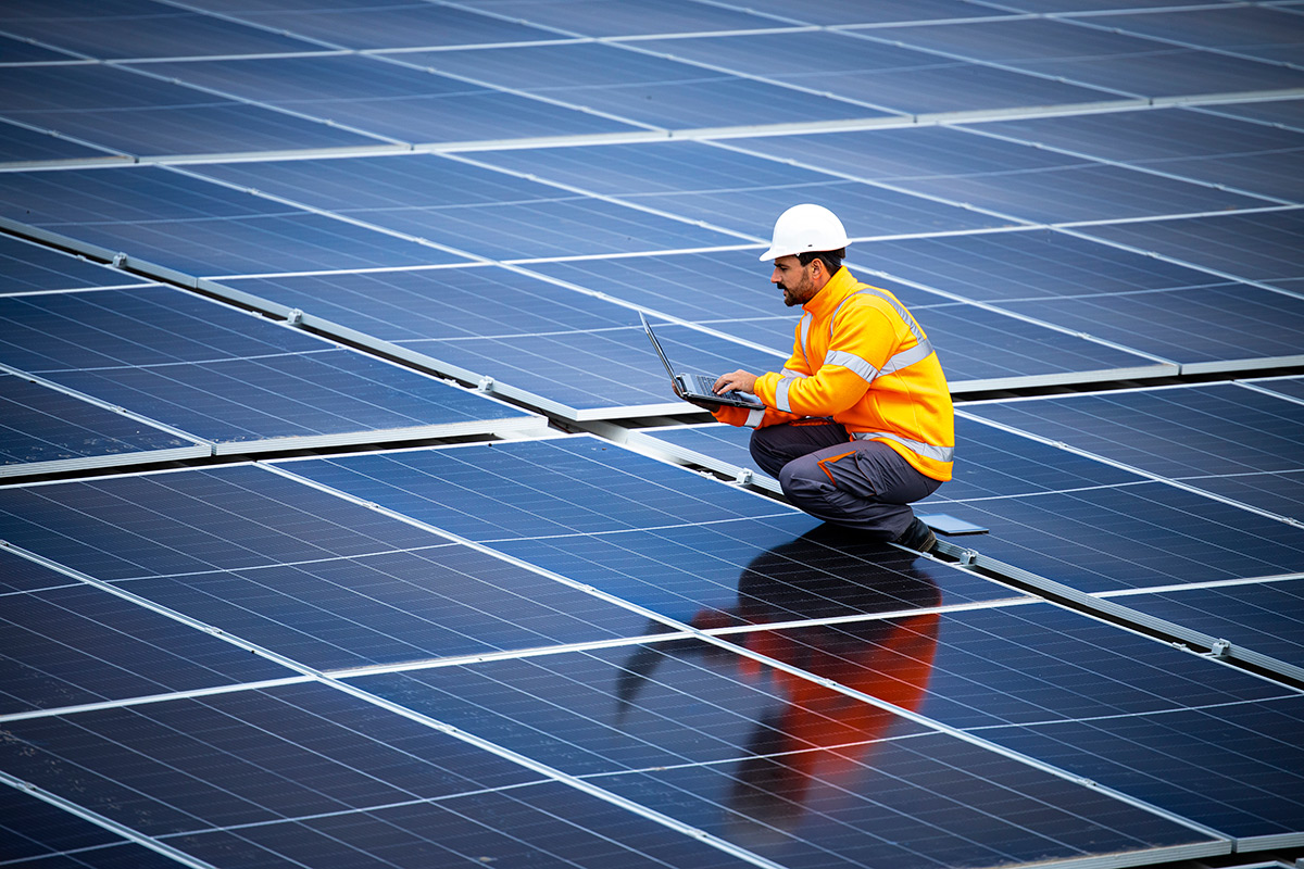 Solar energy plant engineer standing between photovoltaic panels and checking electricity production for industry.