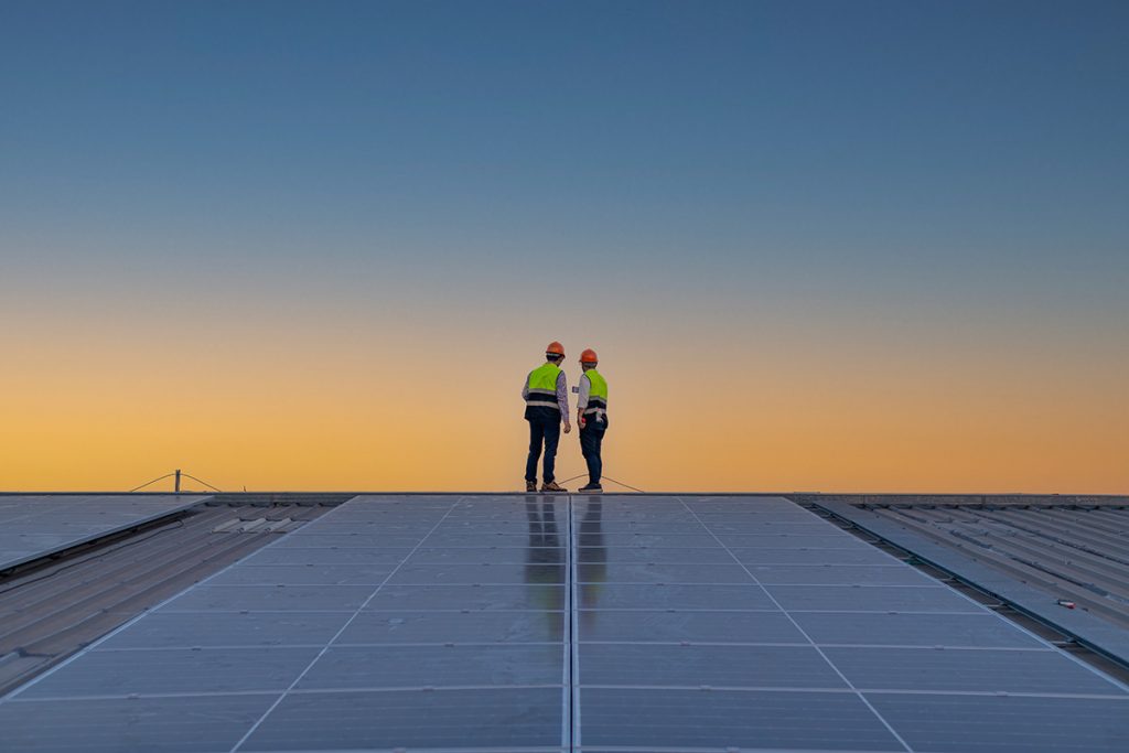 Two workers standing in a roof with solar panels