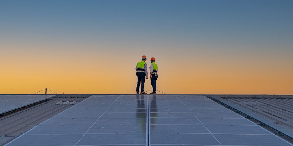 Two workers standing in a roof with solar panels