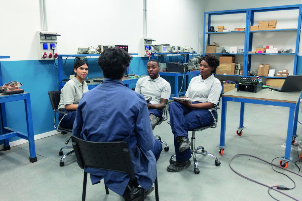 A male professoris instructing a multi racial goup of students using a digital tablet after a practice at a technical school